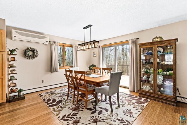 dining area featuring light wood-style floors, a textured ceiling, a wall unit AC, and baseboard heating