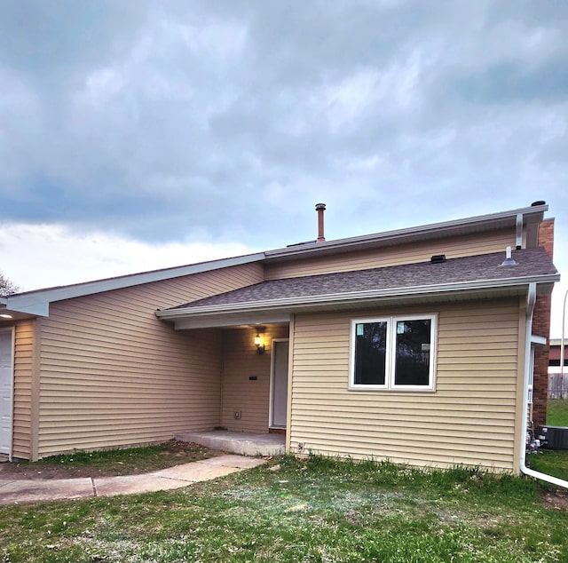 view of front facade featuring a front lawn, roof with shingles, and central AC