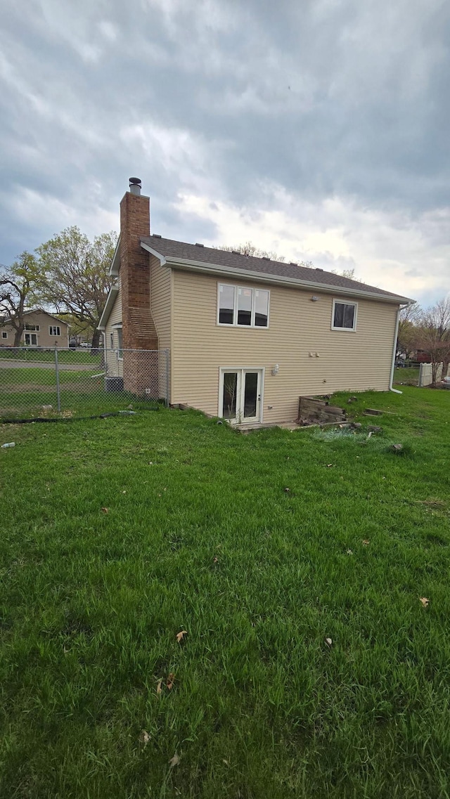 rear view of house featuring fence, a chimney, and a yard
