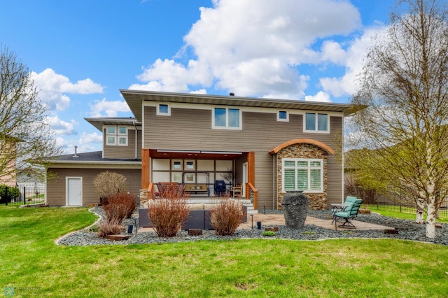 rear view of property featuring a yard, a patio area, stone siding, and fence