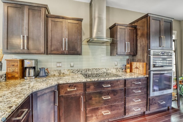 kitchen featuring light stone counters, dark wood finished floors, wall chimney range hood, black electric cooktop, and double oven