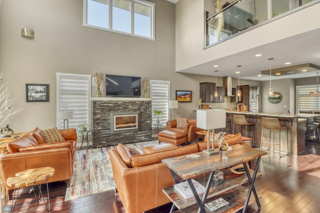 living room featuring dark wood-type flooring, a towering ceiling, and a stone fireplace