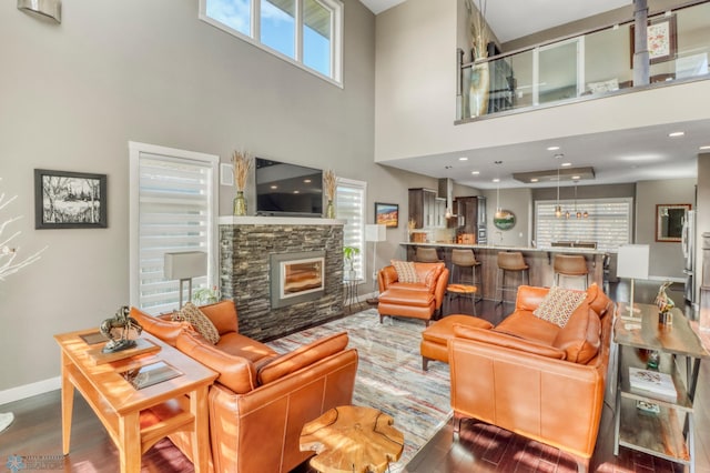 living room featuring a high ceiling, wood finished floors, baseboards, and a stone fireplace