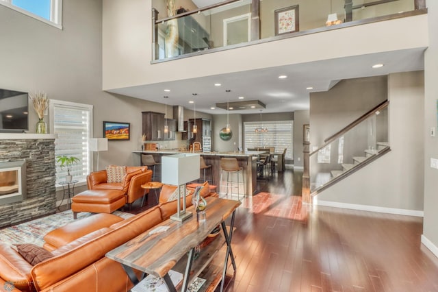 living room featuring a stone fireplace, baseboards, dark wood-style floors, and a towering ceiling