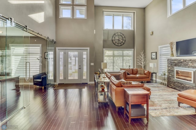 living area with dark wood-style flooring, a towering ceiling, baseboards, and a stone fireplace