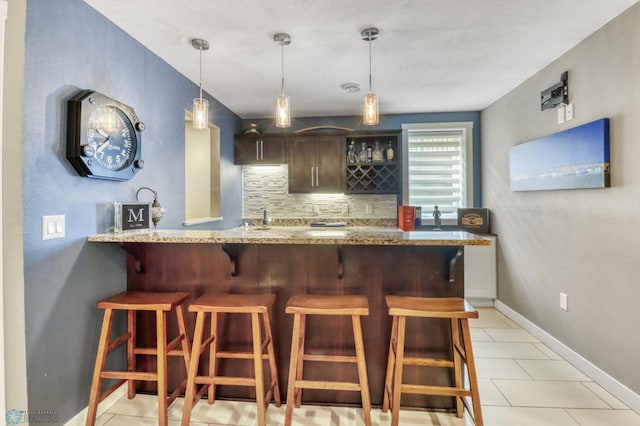 bar with hanging light fixtures, light tile patterned floors, indoor wet bar, baseboards, and decorative backsplash