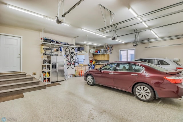 garage with stainless steel refrigerator with ice dispenser and a garage door opener