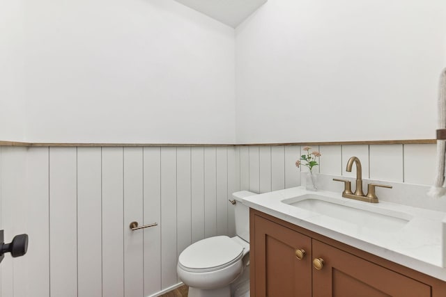 half bathroom featuring toilet, vanity, and wainscoting