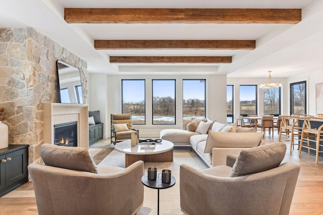 living room with beamed ceiling, a chandelier, a glass covered fireplace, and light wood-type flooring