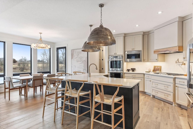 kitchen featuring stainless steel appliances, light countertops, decorative backsplash, a sink, and light wood-type flooring