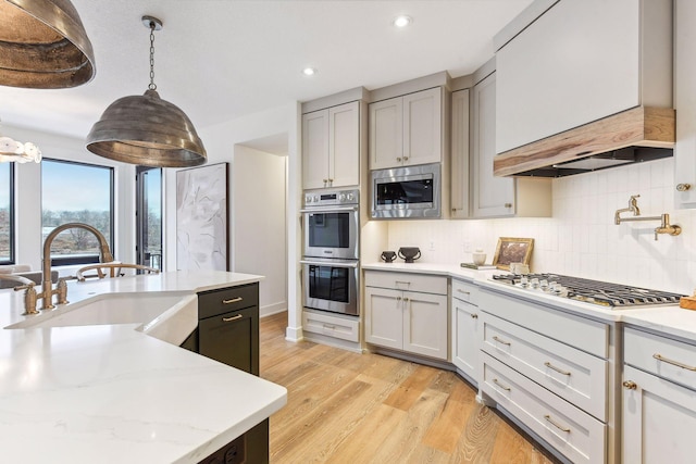 kitchen featuring stainless steel appliances, a sink, light wood-style flooring, decorative backsplash, and recessed lighting