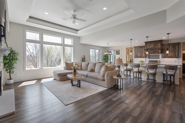 living area with a ceiling fan, dark wood finished floors, baseboards, a tray ceiling, and recessed lighting