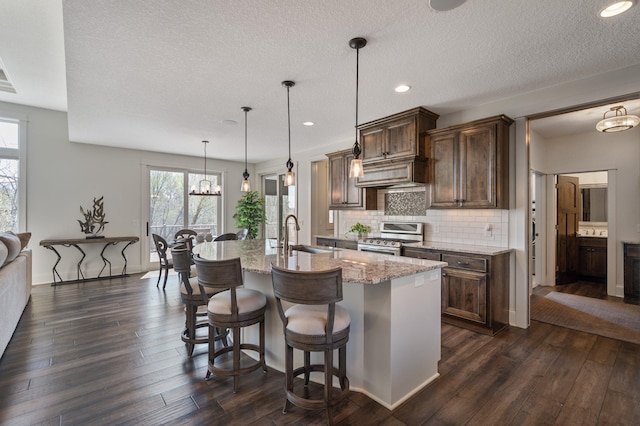 kitchen with light stone counters, decorative backsplash, dark wood-style floors, and stainless steel gas range