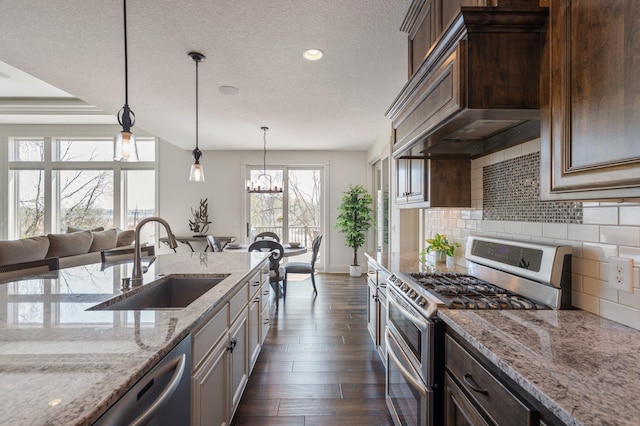 kitchen with light stone counters, appliances with stainless steel finishes, a sink, tasteful backsplash, and custom exhaust hood