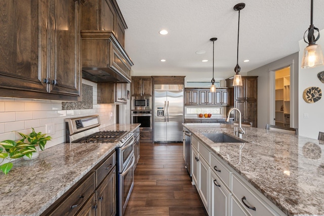 kitchen with pendant lighting, built in appliances, dark wood-style floors, light stone counters, and a sink