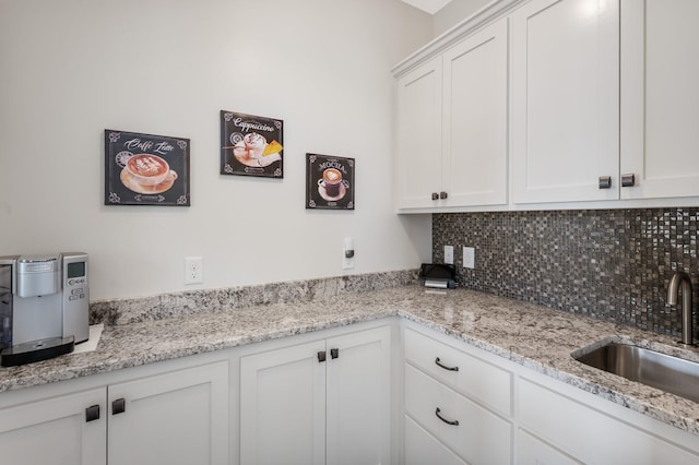 kitchen featuring a sink, white cabinets, light stone countertops, and tasteful backsplash