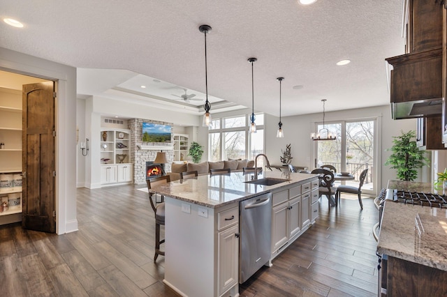 kitchen featuring stainless steel dishwasher, open floor plan, dark wood-type flooring, a sink, and ceiling fan with notable chandelier