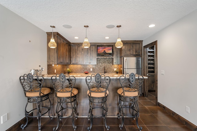 kitchen with backsplash, a peninsula, baseboards, and dark tile patterned floors