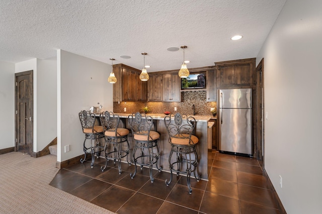 kitchen featuring freestanding refrigerator, pendant lighting, a peninsula, a breakfast bar, and tasteful backsplash