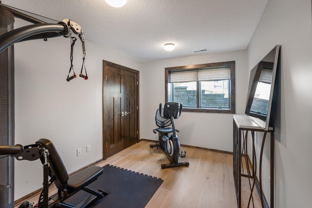 exercise room featuring baseboards, light wood finished floors, a textured ceiling, and visible vents