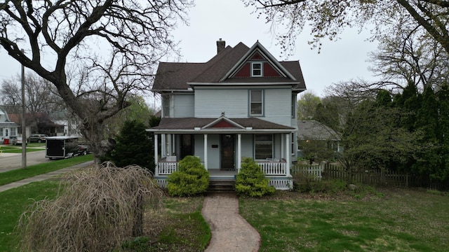 victorian home featuring a porch, a chimney, a front yard, fence, and a shingled roof