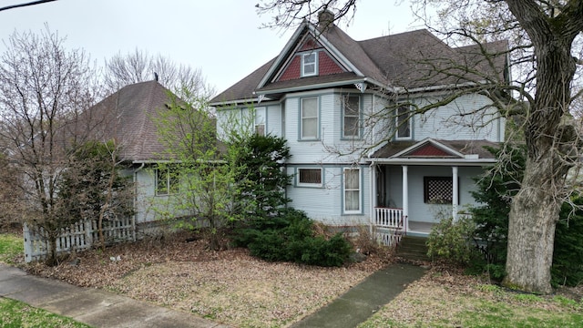 victorian house with a shingled roof, covered porch, and a chimney