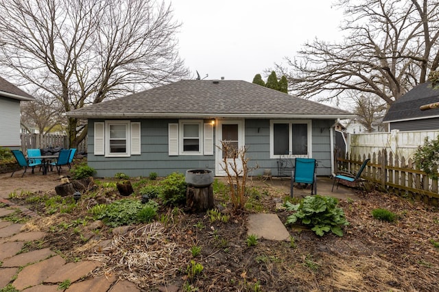 rear view of house featuring fence, a shingled roof, and a patio area