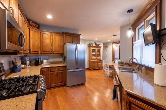 kitchen featuring appliances with stainless steel finishes, a sink, brown cabinetry, light wood-style flooring, and decorative light fixtures
