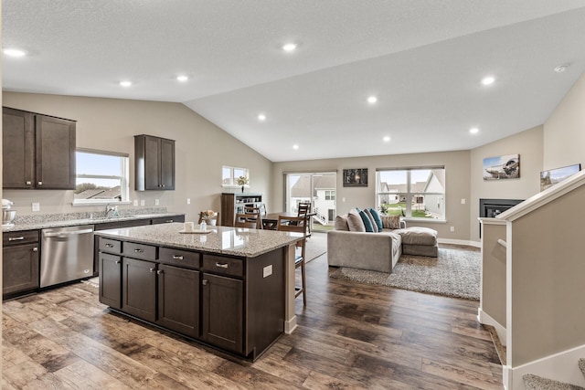kitchen with a sink, a healthy amount of sunlight, stainless steel dishwasher, vaulted ceiling, and a kitchen island