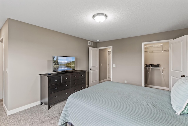 carpeted bedroom with a textured ceiling, baseboards, a spacious closet, visible vents, and a closet