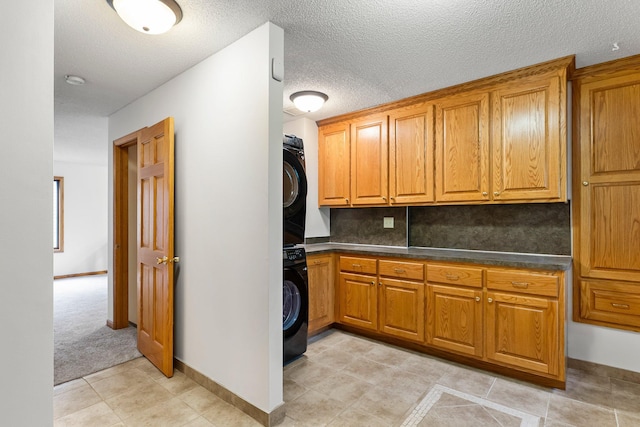 7884 341st St, Lent Twp, MN 55079 - kitchen featuring stacked washer / dryer, brown cabinetry, dark countertops, light tile patterned floors, and a textured ceiling