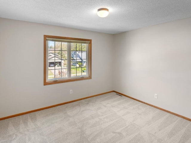 empty room with carpet, baseboards, and a textured ceiling