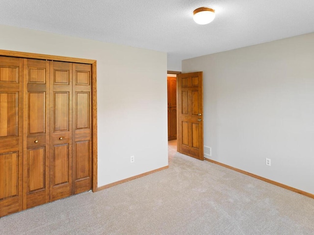 unfurnished bedroom featuring light colored carpet, baseboards, a closet, and a textured ceiling