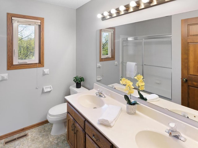 full bath featuring baseboards, a stall shower, toilet, and double vanity