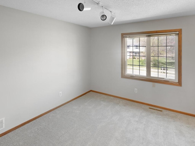 unfurnished room with rail lighting, carpet flooring, baseboards, and a textured ceiling