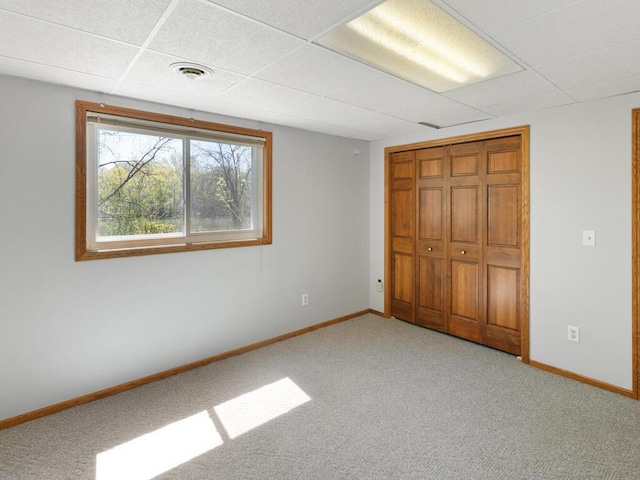 unfurnished bedroom featuring carpet flooring, baseboards, a closet, and a paneled ceiling