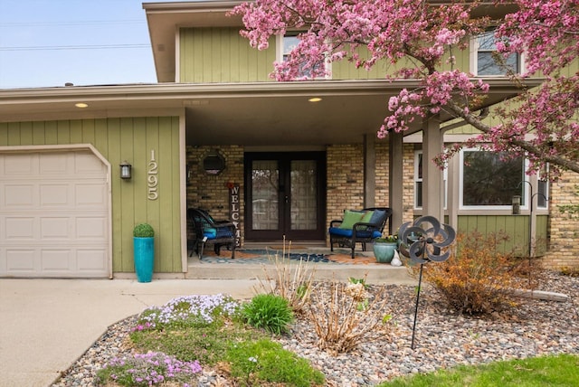 property entrance with a porch, brick siding, french doors, and a garage