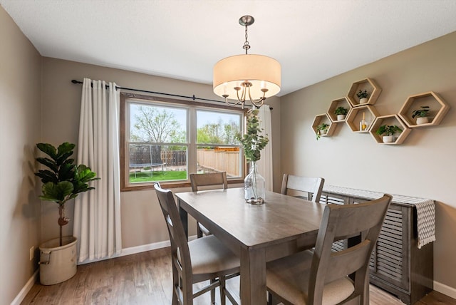dining space with baseboards, light wood finished floors, and a chandelier