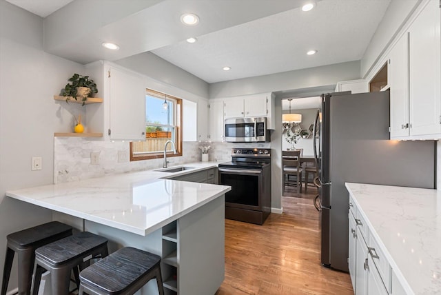 kitchen with open shelves, a peninsula, light wood-style floors, a sink, and stainless steel appliances