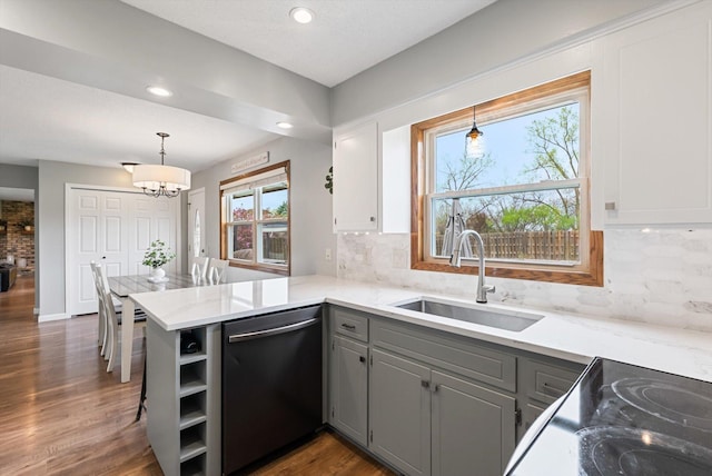 kitchen with open shelves, a peninsula, dishwashing machine, a sink, and gray cabinetry