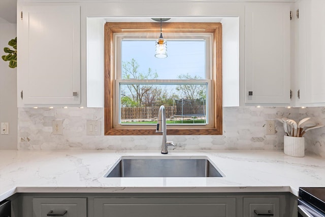 kitchen featuring tasteful backsplash, light stone countertops, a sink, gray cabinetry, and white cabinetry