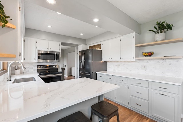 kitchen with a sink, open shelves, appliances with stainless steel finishes, and a peninsula