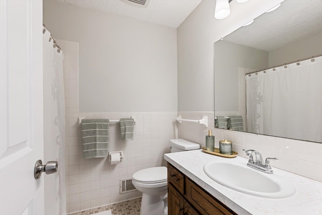 bathroom featuring vanity, visible vents, toilet, tile walls, and a textured ceiling