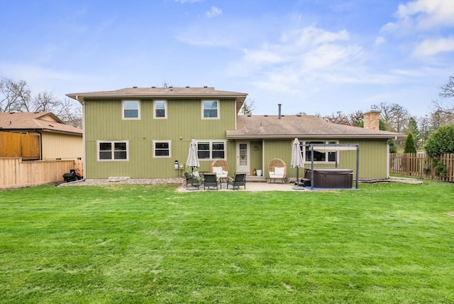 back of property featuring a chimney, a lawn, a hot tub, a fenced backyard, and a patio