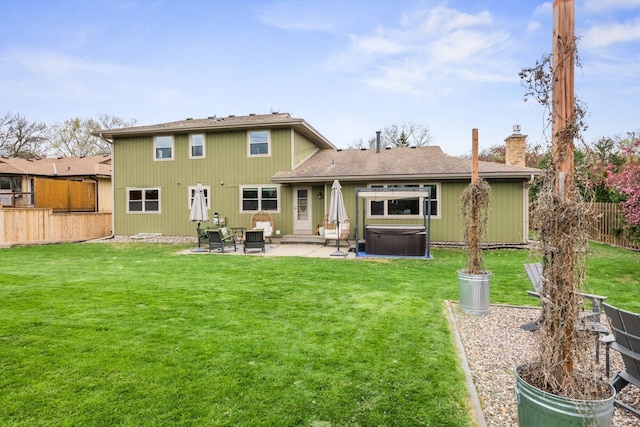 back of property with a fenced backyard, a chimney, a patio area, a hot tub, and a yard