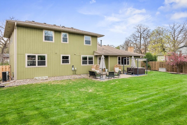 rear view of property featuring a fenced backyard, a yard, a hot tub, and a patio area
