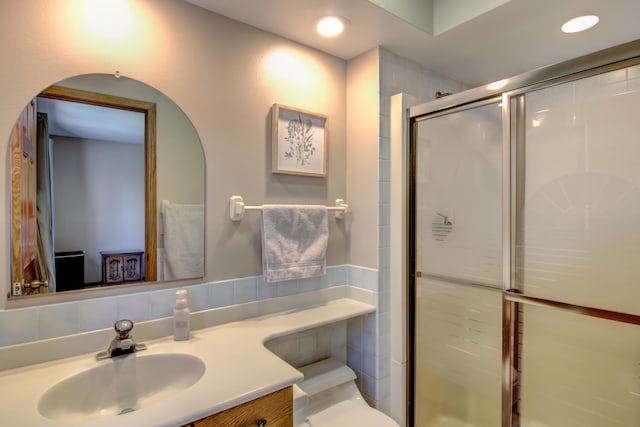 bathroom with tile walls, a stall shower, vanity, toilet, and recessed lighting
