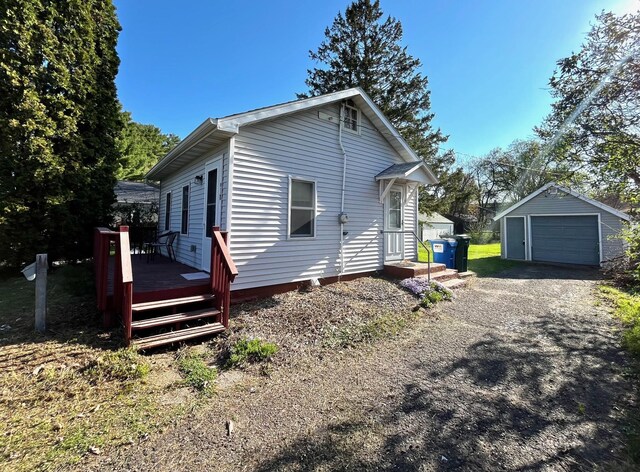 view of side of home featuring a wooden deck, a detached garage, an outdoor structure, and dirt driveway