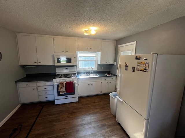 kitchen featuring white appliances, a sink, white cabinets, dark wood-style flooring, and dark countertops