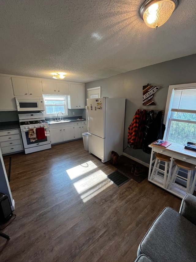 kitchen with white appliances, a textured ceiling, dark wood finished floors, white cabinets, and a sink
